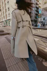 Gabardina larga color beige, con cuello solapa, manga larga con trabillas en hombros y cierre frontal cruzado con botones negros. Incluye cinturón a tono anudado.