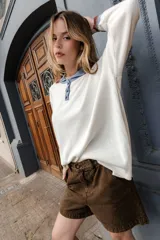 Buzo blanco de algodón con cuello polo con botones, mangas largas con puños acanalados a rayas en tonos marrón y celeste.