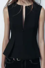 Top color crema, de cuello redondo y sin mangas. Tiene cintura entallada y bajo con pinzas acabado peplum. Cierre frontal con cremallera oculta en costura.