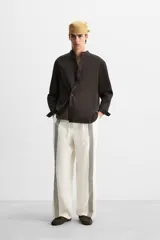 Pantalón relaxed fit confeccionado en tejido de lino color crudo. Cintura elástica ajustable con cordón, bolsillos laterales y traseros. Perneras con aplicación de bandas verticales negras a contraste en delantero.