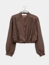 Camisa corta color marrón con cuello mao, mangas largas abullonadas con puños elásticos y cierre frontal con botones.