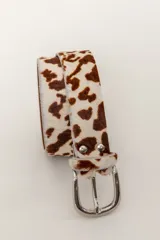 Cinturón con estampado animal print de vaca en tonos marrón y blanco, con hebilla metálica plateada.