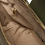 Cartera de mano y hombro color verde oliva, con cuerpo de lona y detalles en cuero sintético (PU) verde oscuro. Presenta un bolsillo frontal con solapa y broche dorado, asas cortas superiores y una correa larga desmontable y regulable. El herraje es dorado y lleva el logo "XL" aplicado al frente.