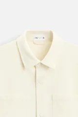 Sobrecamisa negra de tejido con elasticidad, cuello solapa y manga larga acabada en puño con botón a presión. Tiene bolsillos de plastrón en el pecho y cierre frontal con botones a presión.