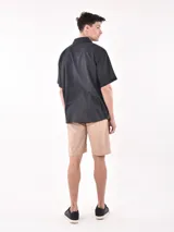 Camisa de manga corta color negro, con cuello camisero y un bolsillo de parche en el pecho izquierdo. Presenta un corte holgado (oversize).