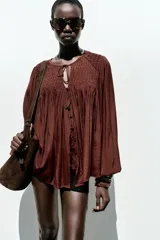 Blusa marrón con cuello redondo con cordón con abalorios, escote pico y manga larga abullonada. Cierre frontal con botones forrados a tono.