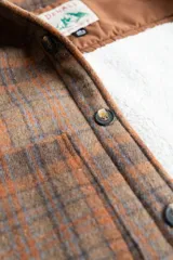 Camisa leñadora a cuadros marrón y naranja, forrada en corderito sintético, con cuello clásico, cierre frontal con botones, dos bolsillos frontales con tapa y puños abotonados.