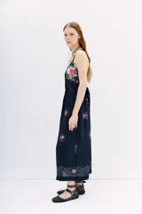 Vestido midi negro con estampado floral y puntos blancos. Presenta escote pronunciado en la espalda con múltiples tiras finas cruzadas que se atan con un lazo en la cintura.