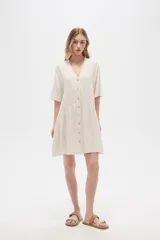 Vestido corto color crema, de corte holgado, con cuello en V y botones frontales.