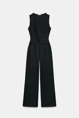 Mono largo negro de crepe, sin mangas, con escote en V y detalle superpuesto tipo chaleco cruzado con un botón. Presenta pierna ancha y cierre frontal.