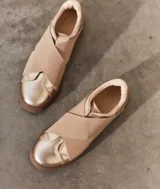 Zapatillas slip-on doradas con banda elástica cruzada en color beige.