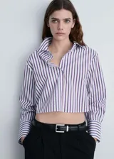 Camisa crop de rayas verticales blancas y azules, con cuello camisero, cierre frontal con botones, mangas largas con puños abotonados y corte regular.