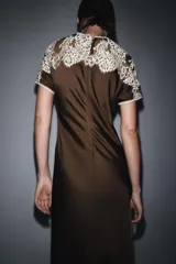 Vestido midi de viscosa color marrón oscuro, con cuello redondo y manga corta. Presenta un canesú de encaje floral color beige claro que cubre los hombros y parte superior del pecho. El bajo es evasé.