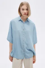 Camisa celeste de manga corta, corte holgado, con cuello camisero y cierre frontal con botones.