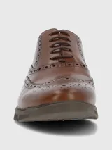 Zapato de vestir tipo Oxford o Brogue, color marrón cuero, con puntera y laterales decorados con perforaciones (broguing). Posee cordones y una suela de goma gruesa y moderna de color marrón oscuro.