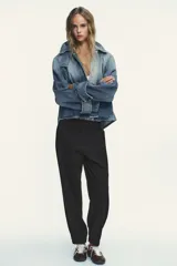 Chaqueta de denim celeste con cuello alto, manga larga con trabilla y bolsillos laterales. Presenta detalle de pliegues en la espalda y cierre frontal con botones ocultos.