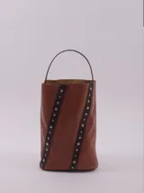 Bolso matero color marrón de cuero con manija rígida superior y correa larga desmontable. Presenta dos tiras de cuero diagonales con tachas plateadas.