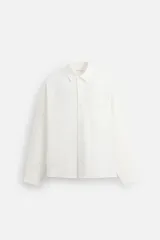Camisa blanca de corte regular fit, confeccionada en tejido de mezcla de algodón. Tiene cuello italiano, manga larga con puños abotonados, bolsillo de parche en el pecho y cierre frontal con botones.