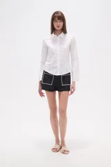 Camisa blanca de algodón, entallada, con cuello camisa y cierre frontal de botones. Presenta mangas largas con puños sencillos.