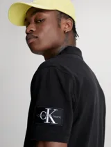 Chomba negra de piqué de algodón peinado, corte regular, cuello clásico con dos botones, mangas cortas, dobladillo con aberturas laterales y logo de Calvin Klein en la manga.