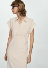 Vestido color crema de tejido fluido, con cuello camisero, mangas cortas con vuelta, detalles drapeados, diseño midi y entallado, y cierre delantero de botones oculto.