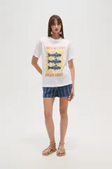 Remera blanca de algodón con cuello redondo y mangas cortas. Estampado frontal con diseño de peces azules sobre fondo a cuadros amarillos y texto "Isola di Capri" y "Amalfi Coast".