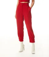 Pantalón zanahoria de vestir color rojo con cintura alta, trabillas, cierre con doble botón, bolsillos laterales, pliegues frontales y botones decorativos en los tobillos.