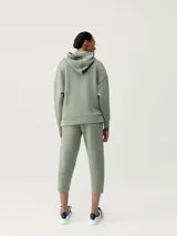 Buzo con capucha color verde, de tejido técnico, diseño holgado, hombro caído y bolsillos.