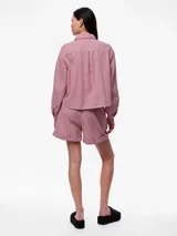 Camisa de denim a rayas verticales rojas y blancas, con cuello clásico, cierre frontal con botones plateados, mangas largas con puños abotonados, bolsillo de parche en el pecho y corte holgado.