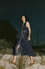 Vestido midi azul marino con estampado de lunares blancos, cuello solapa, escote en pico y sin mangas. Incluye cinturón de la misma tela y cierre frontal con botones.