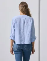 Blusa de algodón a rayas verticales finas en tonos blanco y lila, con escote en V, abertura frontal con botones y mangas largas regulables con presilla y botón. El ruedo termina anudado al frente.