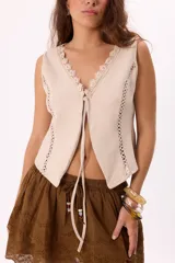 Chaleco color crema con escote en V y cierre frontal con lazos. Presenta detalles de puntilla en el escote y calados en los laterales.