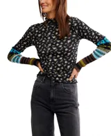 Top de manga larga ajustado, color negro con estampado floral pequeño en tonos beige y amarillo. Presenta cuello alto tipo mock con borde festoneado y puños alargados de punto con diseño multicolor a rayas y patrones geométricos en tonos azul, verde, marrón y negro.