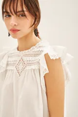 Camisa blanca de algodón con detalles de puntilla en el canesú, volados con terminación de puntilla en las mangas y cartera de botones en la parte superior de la espalda.