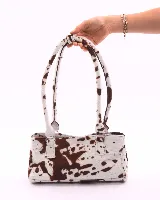 Cartera baguette de cuero con estampado animal print de vaca en tonos marrón y blanco. Tiene forro interior, un bolsillo amplio y broches laterales para ajustar el tamaño.