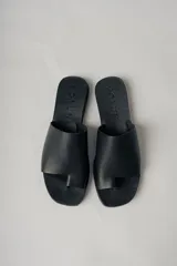 Sandalias planas de cuero color negro, con tira ancha sobre el empeine y diseño minimalista.