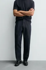 Pantalón de denim azul oscuro, corte wide fit, largo cropped, con pliegues frontales, bolsillos laterales y traseros asimétricos. Cierre frontal con cremallera y gancho metálico oculto.