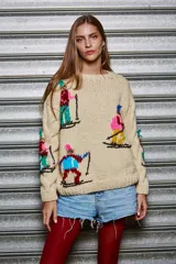 Sweater tejido de lana color beige con cuello redondo y mangas largas. Presenta bordados de figuras esquiando en distintos colores.