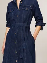 Vestido camisero midi de denim azul oscuro, con cuello clásico, manga tres cuartos y cierre frontal con botones. Incluye cinturón de la misma tela para ajustar a la cintura y dos bolsillos de parche con solapa en el pecho.