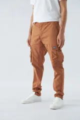 Pantalón cargo color marrón, corte slim, con cierre y botón en la cintura, pasacintos y bolsillos cargo con botones.