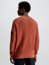 Sweater de punto texturizado color ladrillo, con cuello redondo, mangas largas raglán y logo de Calvin Klein en la manga.
