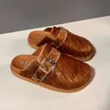 Mules negros de cuero con hebilla metálica y detalle de pelo en la parte superior.