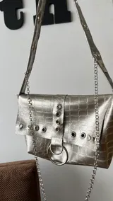 Cartera negra con textura símil cocodrilo, con herrajes plateados y cadena decorativa.