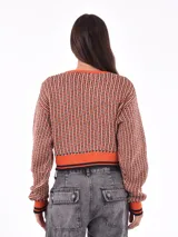 Cárdigan tejido con patrón geométrico en tonos naranja, negro y blanco. Tiene cuello en V, cierre con botones negros y ribetes a contraste en cuello, puños y bajo.