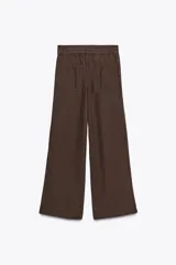 Pantalón marrón de tiro medio, corte ancho y largo cropped. Confeccionado en algodón, con cintura con trabillas y elástico en la espalda, bolsillos laterales y traseros, pinzas en el delantero y cierre frontal con cremallera, botón y ganchos metálicos.