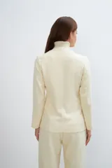 Chaqueta corta color beige, entallada, con escote en V, manga larga y cierre frontal con lazo fijo. Confeccionada en lana fina sin teñir, con bolsillos escondidos y terminaciones enviadas. Hecha 100% en Uruguay.