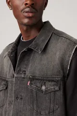 Chaleco de jean negro gastado, con cuello clásico, cierre frontal con botones metálicos, bolsillos con solapa en el pecho y corte recto.