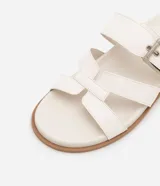Sandalias planas de cuero sintético color blanco, con puntera redonda y dos tiras, una con hebilla metálica y otra en forma de H.