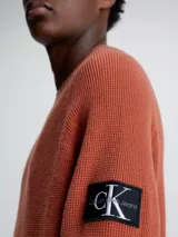 Sweater de punto texturizado color ladrillo, con cuello redondo, mangas largas raglán y logo de Calvin Klein en la manga.