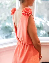 Vestido largo color rosa pálido, con escote en V cruzado, sin mangas y cinturón negro con apliques de flores. Presenta detalle de volados en los hombros y corte evasé.